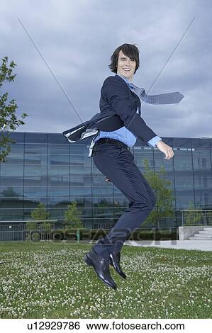 Businessman in park jumping in air office in background. View Large Photo Image Stock Photograph - Businessman in park jumping in air office in background.. Fotosearch