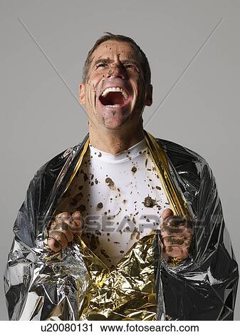 Stock Image - Mud covered man with thermal blanket. Fotosearch