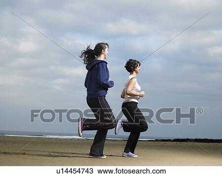 Stock Image - Two young females jogging on beach. Fotosearch