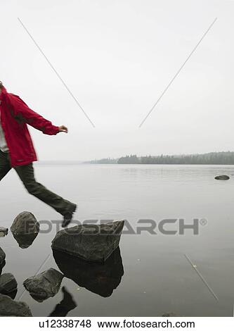 Stock Photo - Woman jumping onto a rock in the water.. Fotosearch