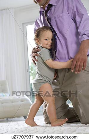 Stock Photo - Baby hugs fathers legs and smiles. Fotosearch