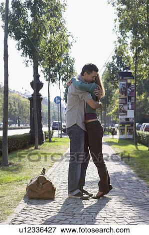 Stock Photo - Couple embracing on a sidewalk smiling.. Fotosearch