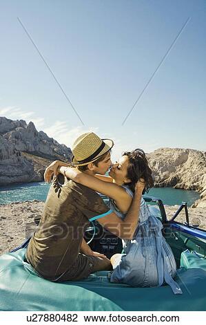 Stock Image - Man and woman sitting on car.. Fotosearch