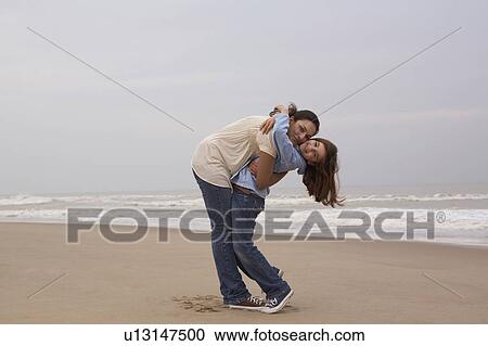 Stock Image - Mother embracing daughter (9-11) on beach, portrait. Fotosearch