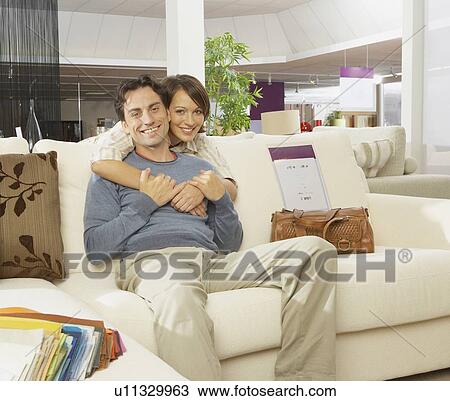 Stock Image - Smiling couple on sofa in furniture shop.. Fotosearch