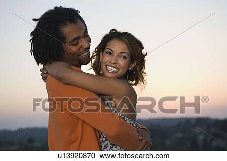 Stock Image - Young man and woman hugging at sunset. Fotosearch