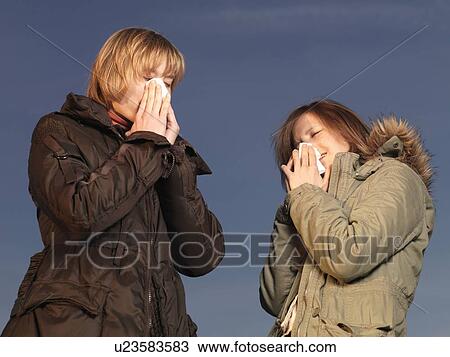 Stock Image - Two women blowing noses into tissues. Fotosearch
