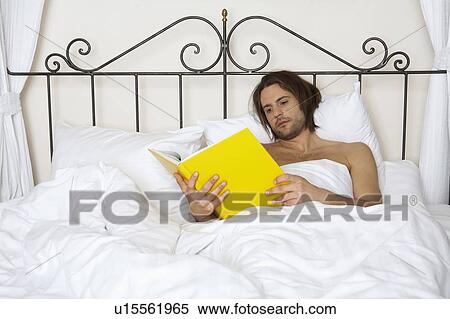 Stock Photography - young man lying in bed holding yellow book. Fotosearch