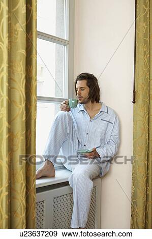 young man sitting on window sill wearing pyjamas holding cup of coffee View Large Photo Image Stock Photo - young man sitting on window sill wearing pyjamas holding cup of coffee. Fotosearch