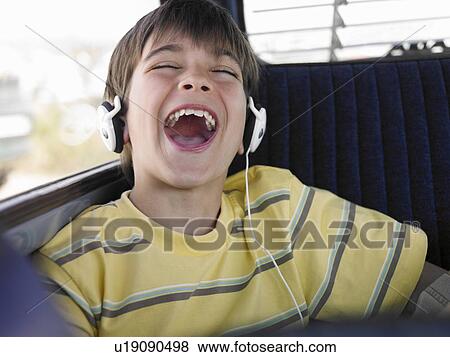 Stock Photo - Boy (8-10) listening to music with headphones in backseat of car, singing. Fotosearch