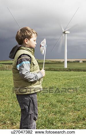 Stock Image - Boy blowing windmill on a wind farm. Fotosearch
