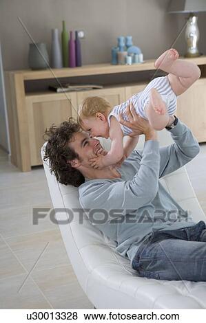 Father holds up baby in chair home View Large Photo Image Stock Photo - Father holds up baby in chair home. Fotosearch