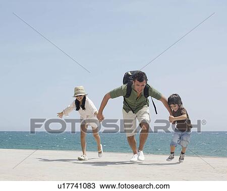 Stock Image - Father running with children by sea. Fotosearch