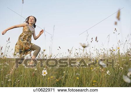Stock Image - Girl runs through field, looks at sun. Fotosearch
