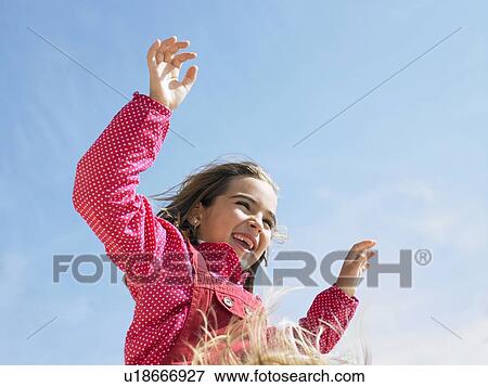 Stock Photo - Low angle view of young girl (5-7) with arms raised on shoulders.. Fotosearch