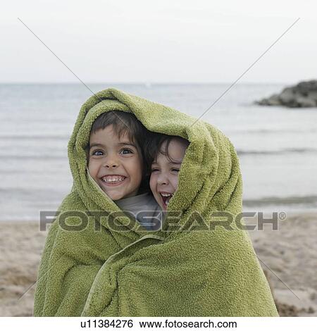 Stock Photograph - Two young children in towel on beach. Fotosearch