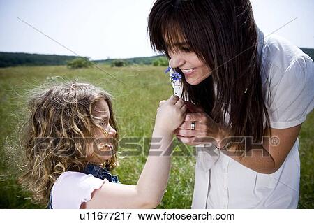 Stock Photo - Woman smelling flower with daughter. Fotosearch
