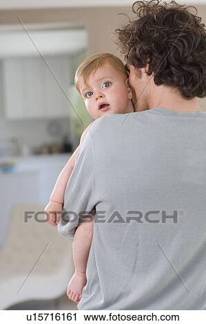 Stock Image - Father cuddles baby at home. Fotosearch