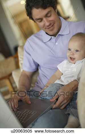 Stock Photography - Father sitting at laptop holding baby. Fotosearch
