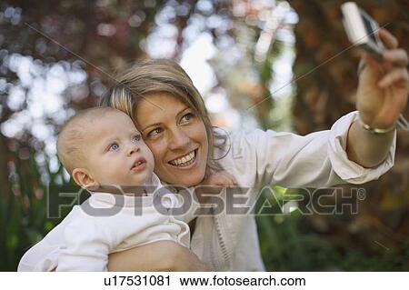 Stock Image - Mother taking picture with baby outdoors. Fotosearch