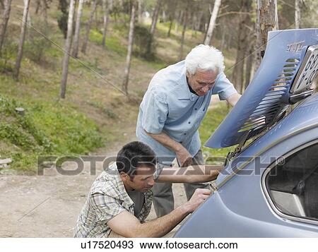 Stock Image - Senior man and adult son fixing car engine on country road, side view. Fotosearch