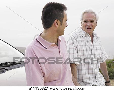 Stock Photo - Senior man and adult son standing beside car at beach, talking. Fotosearch