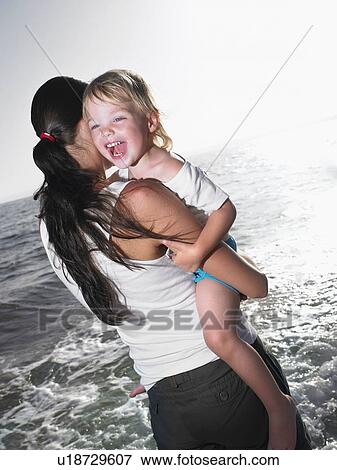 Stock Photo - Woman holding a smiling young girl at the beach.. Fotosearch