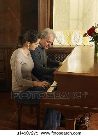 Stock Photography - Young woman playing duet with grey haired man on grand piano. Alicante, Spain.. Fotosearch