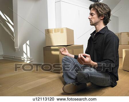 Stock Image - Man doing yoga with moving boxes around him.. Fotosearch