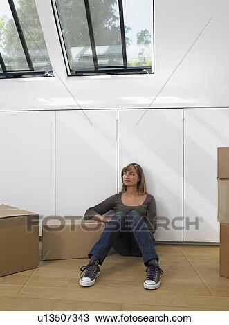 Stock Image - Woman sitting with moving boxes in new home.. Fotosearch