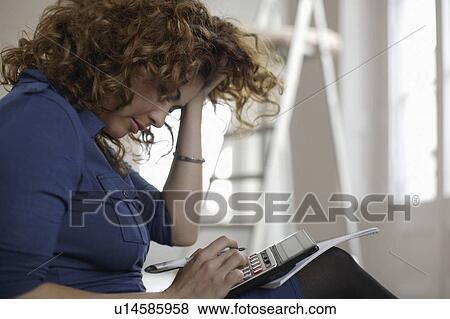 Stock Photo - Woman using calculator in room. Fotosearch