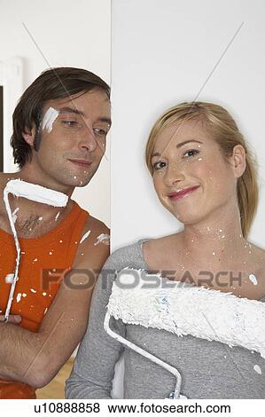 Stock Photo - Young couple holding paint rollers, smiling. Fotosearch