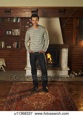 Stock Photo - Young man standing in living room, smiling, portrait. Fotosearch