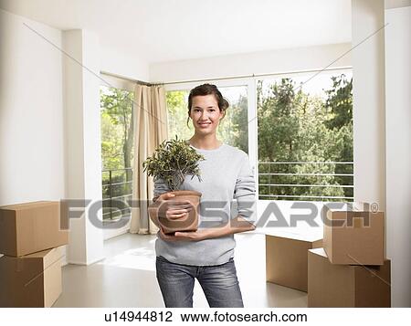 Young woman holding a flowerpot, indoors View Large Photo Image Stock Image - Young woman holding a flowerpot, indoors. Fotosearch