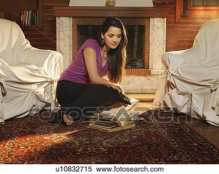 Stock Photography - Young woman sitting on rug in front of fire reading book. Fotosearch