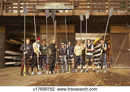 Stock Image - Crew outside boat shed holding blades.. Fotosearch