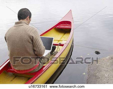 Stock Image - Man sitting in a boat with a laptop.. Fotosearch