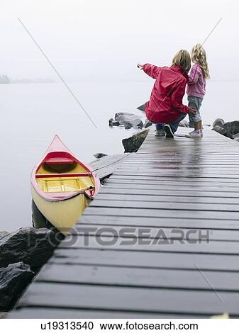 Stock Image - Woman and young girl on a dock near a boat pointing.. Fotosearch
