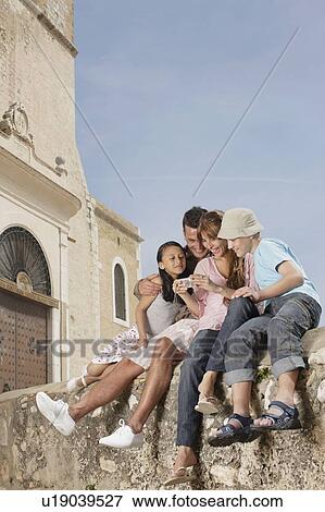 Family sitting on wall sharing photos View Large Photo Image Stock Photo - Family sitting on wall sharing photos. Fotosearch