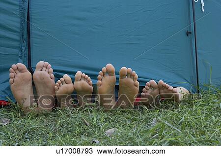 Stock Image - Four people's feet sticking out of tent door.. Fotosearch