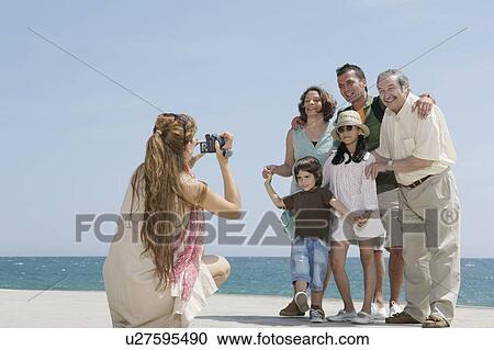 Stock Image - Mother taking video of family by sea. Fotosearch