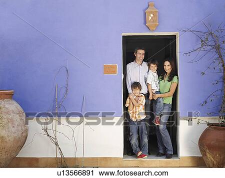 Stock Image - Parents and twin sons (4-6) standing in doorway, smiling, portrait. Fotosearch