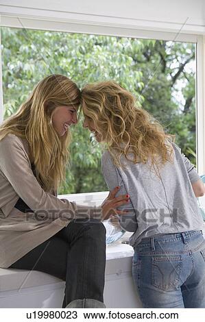 Stock Image - Sisters laughing at kitchen sink. Fotosearch