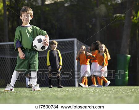 Boy holding soccer ball, children in soccer uniforms in background (portrait) View Large Photo Image Picture - Boy holding soccer ball, children in soccer uniforms in background (portrait). Fotosearch