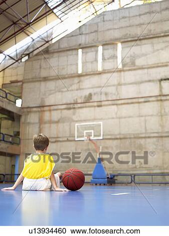 Stock Image - Boy sitting in basketball court (rear view). Fotosearch