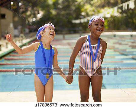 Stock Image - Two girls holding hands by swimming pool. Fotosearch