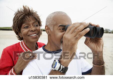 Stock Image - Couple using binoculars at beach. Fotosearch