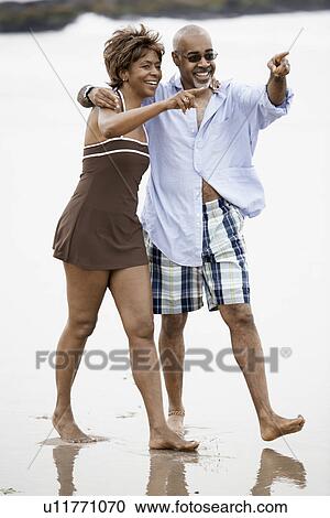 Couple walking and pointing at beach View Large Photo Image Stock Image - Couple walking and pointing at beach. Fotosearch