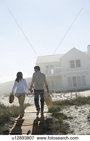 Couple walking towards house on beach View Large Photo Image Stock Photo - Couple walking towards house on beach. Fotosearch