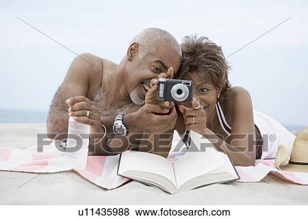 Stock Photo - Mature couple looking at digital camera on beach. Fotosearch